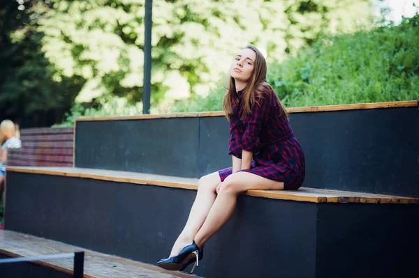 Chica con vestido a cuadros sentado en skatepark mirando a la cámara . — Foto de Stock