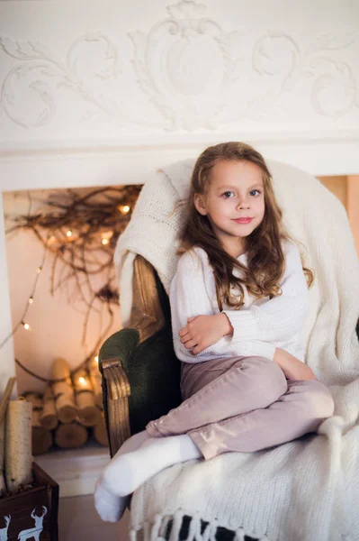 Маленька дівчинка сидить на затишному загорнутому в ковдру кріслі Різдвяна ялинка вранці вдома — стокове фото