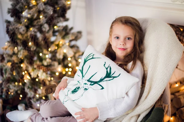 Meisje met Kerstmis, kerstboom op de achtergrond, mooie jonge kind gewikkeld in een deken, ze glimlacht — Stockfoto