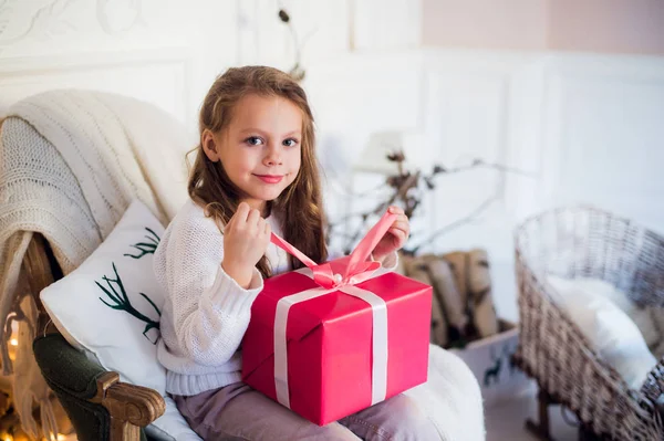Fille heureuse ouvrant cadeaux de Noël par une cheminée décorée dans le salon de lumière confortable la veille de Noël — Photo