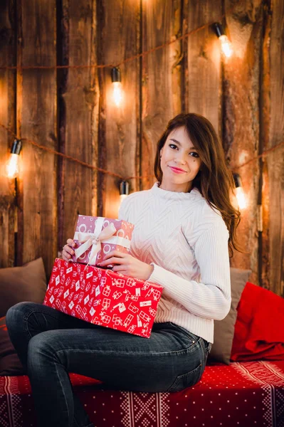 Молода щаслива красива жінка з подарунковими коробками сидить біля стіни, прикрашеної на Різдво в кімнаті будинку. Веселого Різдва та Нового Року . — стокове фото