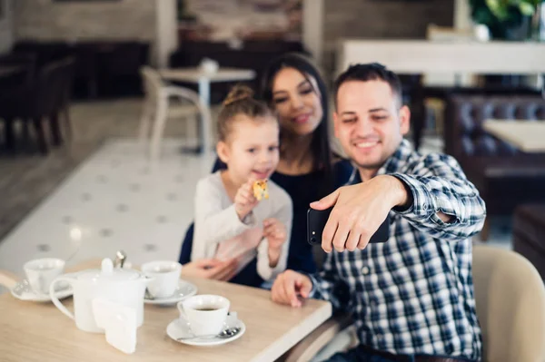 Семья, отцовство, технологии понятие людей - счастливая мать, отец и маленькая девочка обедают, делая селфи на смартфоне в ресторане — стоковое фото