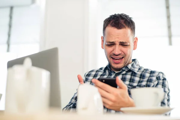 Slecht nieuws. Angry young man houden van een mobiele telefoon en grimassen bij café — Stockfoto