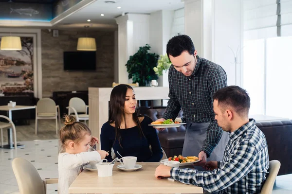 Waiter serving family in a restaurant and bringing full plate — Stock Photo, Image