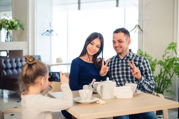 Family, parenthood, technology people concept - close up of happy mother, father and little girl having dinner, kid taking photo by smartphone at restaurant — Stock Photo, Image