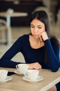 Kız bir kafede oturuyor, elini yanağına aksesuarlar. Yorgun, sakin ifade.