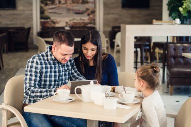 Aile, ebeveynlik, teknoloji insanlar kavramı - mutlu anne, baba ve küçük kız ile tablet pc bilgisayar restoranda akşam yemeği