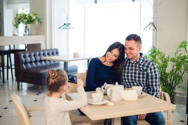 Aile, ebeveynlik, teknoloji insanlar kavramı - mutlu anne, baba ve küçük kız akşam yemeği, çocuk alarak fotoğraf yanında smartphone restoranda yakın