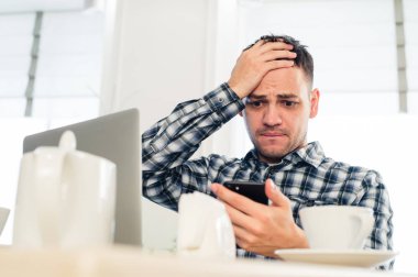 Yorgun yakışıklı genç freelancer kahve dükkanında çalışırken bir cep telefonu kullanarak