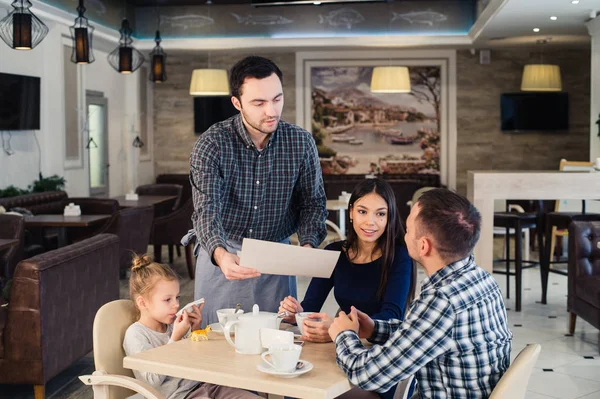 Restaurant en vakantie concept - ober menu geven in Cafe en gelukkige familie — Stockfoto