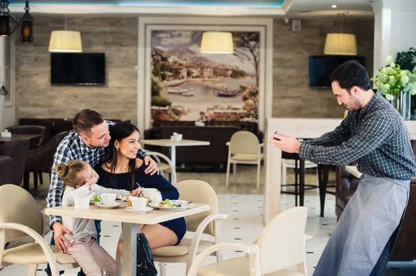 Familia, paternidad, tecnología, concepto de personas - madre feliz, padre y niña cenando pidieron al camarero que tomara una foto por teléfono inteligente —  Fotos de Stock
