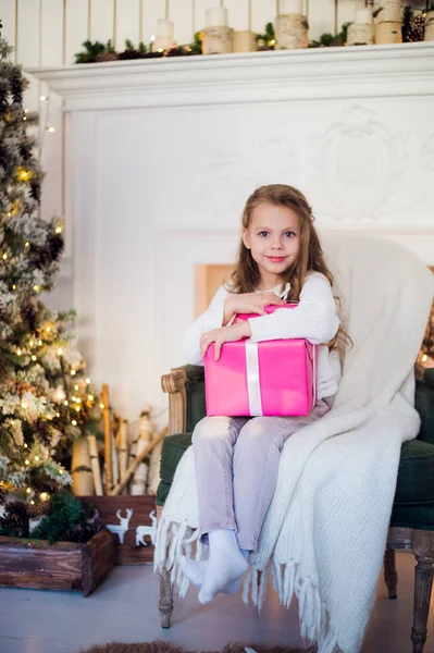 Mooi meisje in de buurt van kerstboom uitpakken presenteert zittend op een stoel — Stockfoto