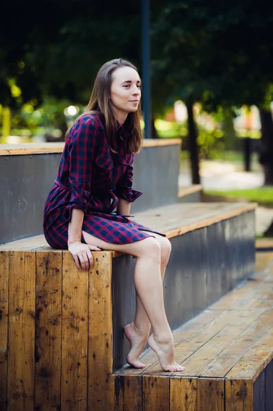 Fille portant une robe à carreaux assis dans skatepark regardant la caméra . — Photo