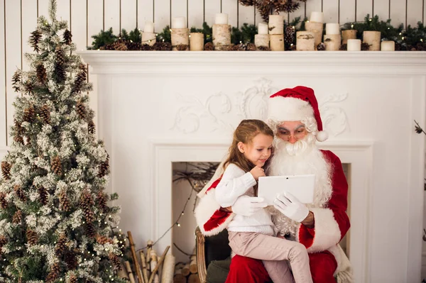 Kerst vakantie blij meisje santa op zoek naar iets op digitale touchscreen tablet Pc, via de schoorsteen en boom kleurrijke verlichting achtergrond. — Stockfoto