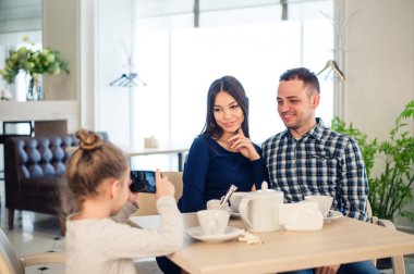 Aile, ebeveynlik, teknoloji insanlar kavramı - mutlu anne, baba ve küçük kız akşam yemeği, çocuk alarak fotoğraf yanında smartphone restoranda yakın