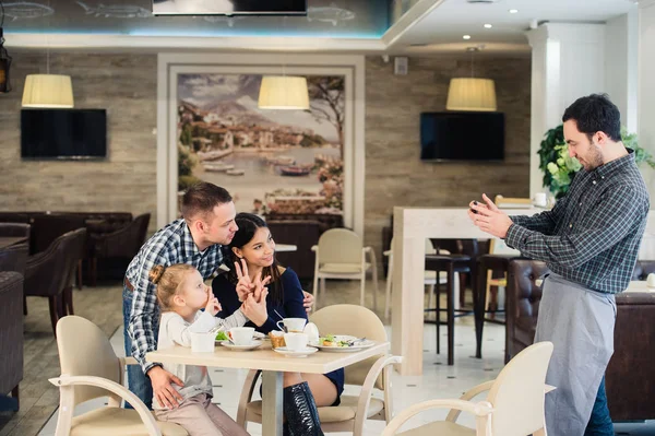 Familia, paternidad, tecnología, concepto de personas - madre feliz, padre y niña cenando pidieron al camarero que tomara una foto por teléfono inteligente —  Fotos de Stock