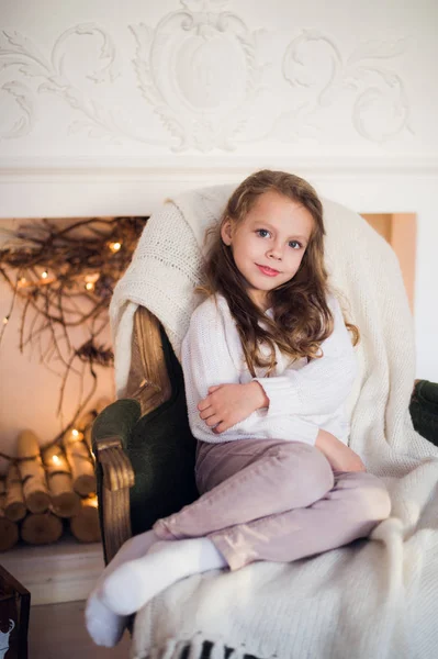 Meisje zittend op gezellige gewikkeld in een deken stoel kerstboom ochtend thuis — Stockfoto