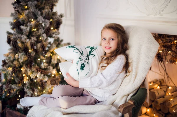 Prinsesje zitten op fauteuil met hert kussen door kerstboom thuis — Stockfoto