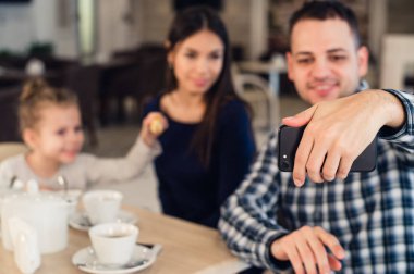 Aile, ebeveynlik, teknoloji insanlar kavramı - mutlu anne, baba ve küçük kız yanında smartphone restoranda selfie alarak yemek yerken