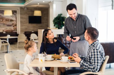 Friendly smiling waiter taking order at table of family having dinner together clipart