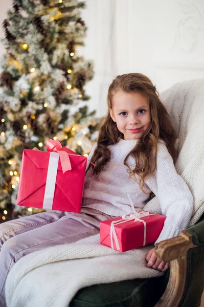Joyeux enfant fille assise sur un fauteuil recouvert d'une couverture contre la cheminée décorée de Noël — Photo