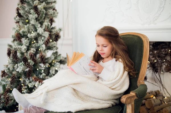 Klein meisje het lezen van boek in de buurt van de kerstboom — Stockfoto