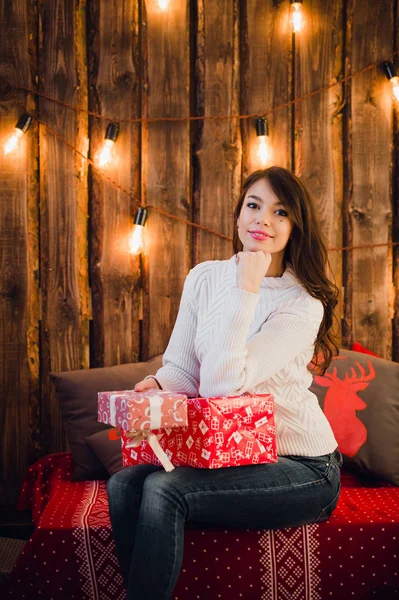 ギフト ボックスを持つ幸せな美しい女は家の部屋でクリスマスの装飾の壁の近くに座っています。メリー クリスマスと新年. — ストック写真