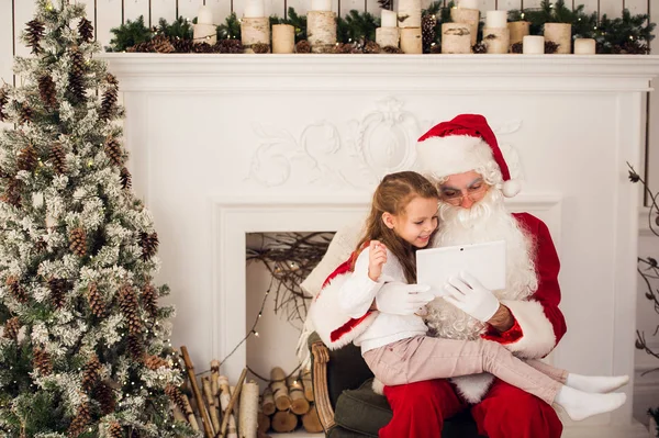 Kerst vakantie blij meisje santa op zoek naar iets op digitale touchscreen tablet Pc, via de schoorsteen en boom kleurrijke verlichting achtergrond. — Stockfoto