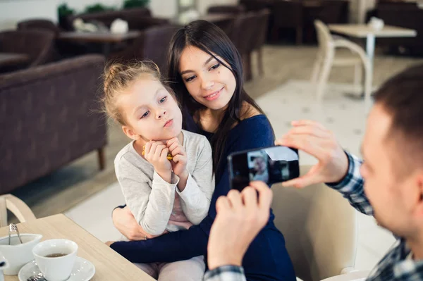 Familia, paternidad, tecnología, concepto de personas - padre feliz tomando fotos de su pequeña hija y esposa por teléfono inteligente cenando en el restaurante — Foto de Stock