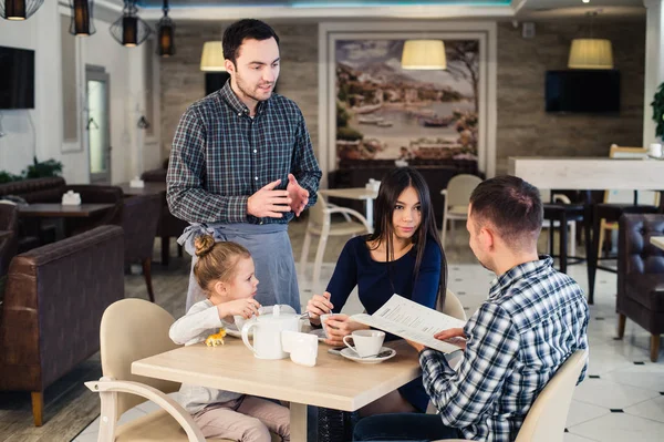 Restaurante y concepto de vacaciones - camarero dando menú a la familia feliz en la cafetería — Foto de Stock