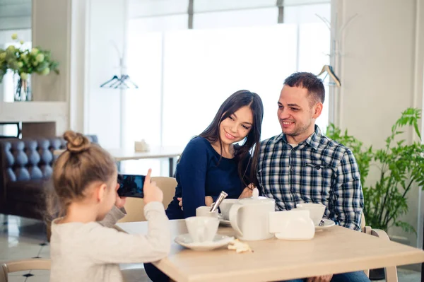 Family, parenthood, technology people concept - close up of happy mother, father and little girl having dinner, kid taking photo by smartphone at restaurant — Stock Photo, Image