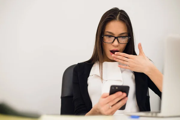 Zbliżenie portret młodego, wstrząśnięty biznes Kobieta, patrząc na telefon komórkowy, widząc, że źle SMS, e-mail, na białym pomieszczeniu biura tle. Negatywne emocje, wyraz twarzy — Zdjęcie stockowe