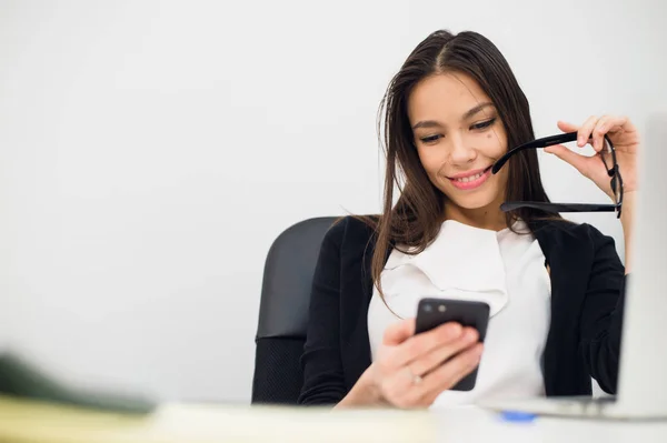 Empresária entusiasmada ganhando após a realização ler telefone inteligente sentado em um desktop no escritório — Fotografia de Stock