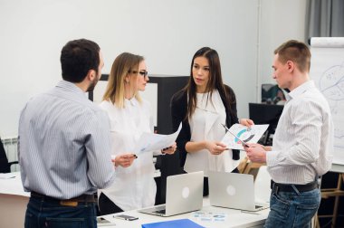 Four young business people working as a team gathered around laptop computer in an open plan modern office clipart