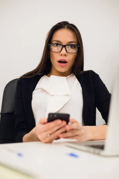 Zbliżenie portret młodego, wstrząśnięty biznes Kobieta, patrząc na telefon komórkowy, widząc, że źle SMS, e-mail, na białym pomieszczeniu biura tle. Negatywne emocje, wyraz twarzy — Zdjęcie stockowe