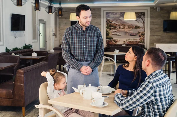 Restaurante y concepto de vacaciones - camarero dando menú a la familia feliz en la cafetería — Foto de Stock