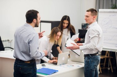 Dizüstü bilgisayar açık plan modern ofis çevresinde toplanan bir ekip olarak çalışma dört genç iş adamları