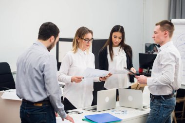 Dizüstü bilgisayar açık plan modern ofis çevresinde toplanan bir ekip olarak çalışma dört genç iş adamları