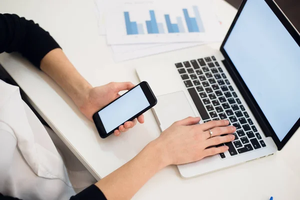 Jonge vrouw met een telefoon. Werkplek in de buurt van het venster met de laptop. Close-up — Stockfoto