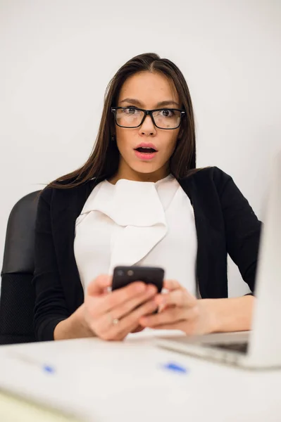 Zbliżenie portret młodego, wstrząśnięty biznes Kobieta, patrząc na telefon komórkowy, widząc, że źle SMS, e-mail, na białym pomieszczeniu biura tle. Negatywne emocje, wyraz twarzy — Zdjęcie stockowe