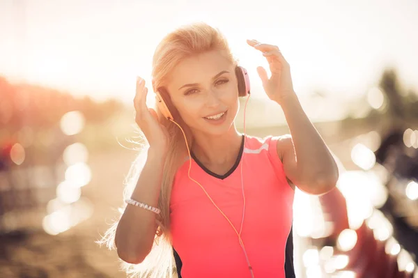 Mujer joven en ropa deportiva disfruta y sonríe escuchando música con auriculares naranjas. Ella pone sus manos arriba disfrutando de la vida . —  Fotos de Stock