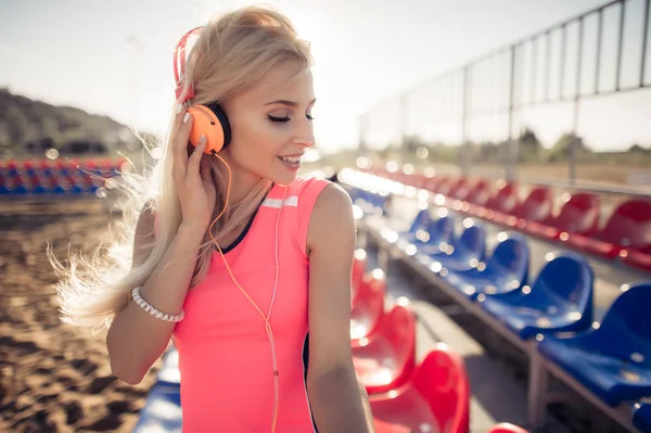 Πορτρέτο του ένα σπορ κορίτσι εφηβικής αναπαύεται από την άσκηση, να ακούτε μουσική με ακουστικά, χαμογελώντας σε εξωτερικούς χώρους. Γυμναστικής και αθλητισμού lifestyle, ηλιόλουστο φωτοβολίδα εξωτερικό. — Φωτογραφία Αρχείου