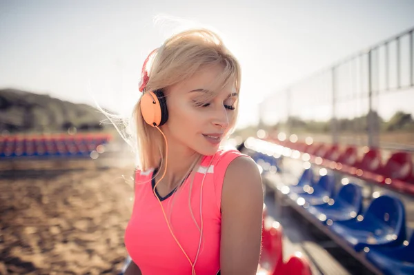 Portret van een sportieve puber meisje rusten uit te oefenen, luisteren naar muziek met koptelefoon, glimlachend buitenshuis. Fitness en sport levensstijl, zonnige flare buitenkant. — Stockfoto