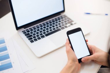 Bir telefon tutan genç kadın. İşyeri dizüstü bilgisayar ile pencere yakınındaki. Yakın çekim