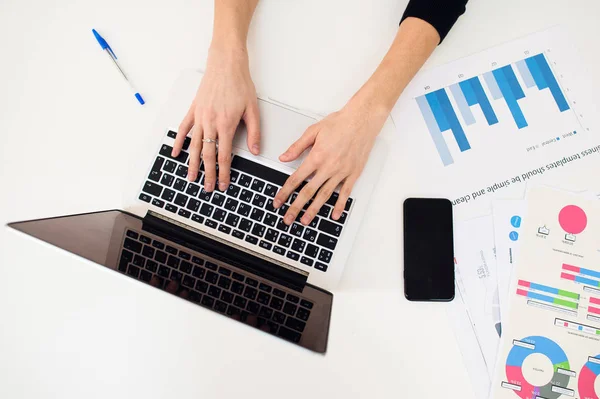 Laptop met vrouwen hand en papier grafiek op witte tafel. — Stockfoto