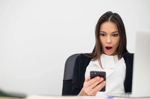 Glædelig overraskende kvinde kigger i mobiltelefon og læser besked med åben mund - Stock-foto