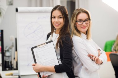 Bir ofiste ayakta ve olumlu klasör evrak tutarken kameraya gülümseyen iki iş kadınları iş arkadaşları