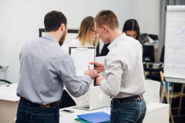 Toplantı ve dizüstü bilgisayarlar kullanarak evraklarla tartışılması sırasında ofisinde oturan genç iş adamları