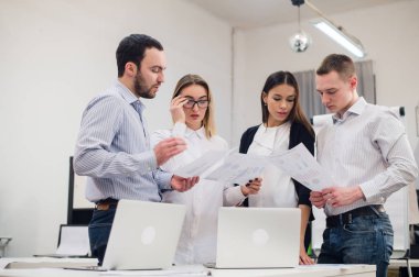 Mükemmel yaratıcı ekibi. Gençlerin grup gülümseme yaslanmış ofiste tabloda için süre ile kameraya bakarak dört neşeli
