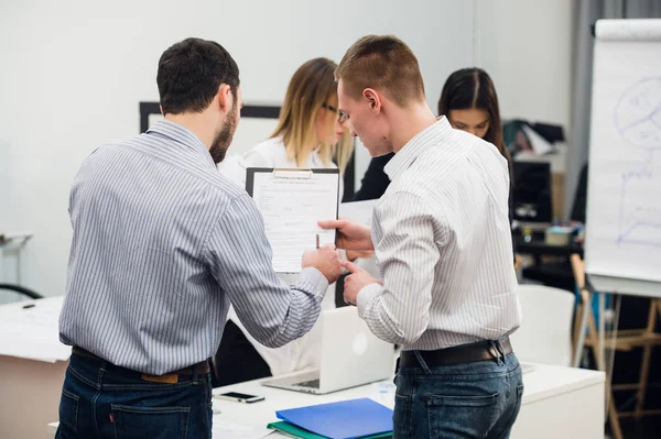 Toplantı ve dizüstü bilgisayarlar kullanarak evraklarla tartışılması sırasında ofisinde oturan genç iş adamları